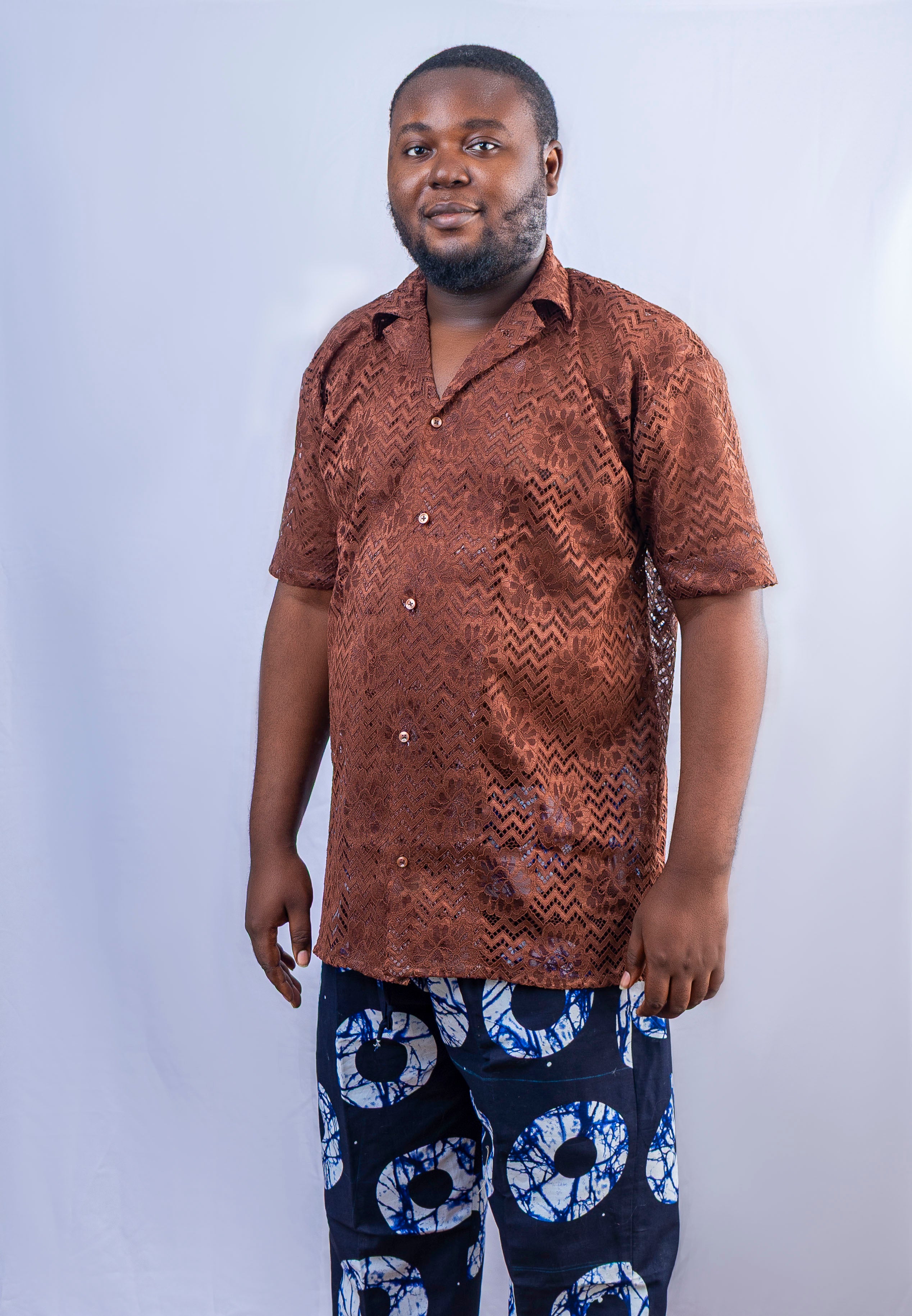 A man wearing a brown patterned short-sleeved button-up shirt and dark blue patterned pants.