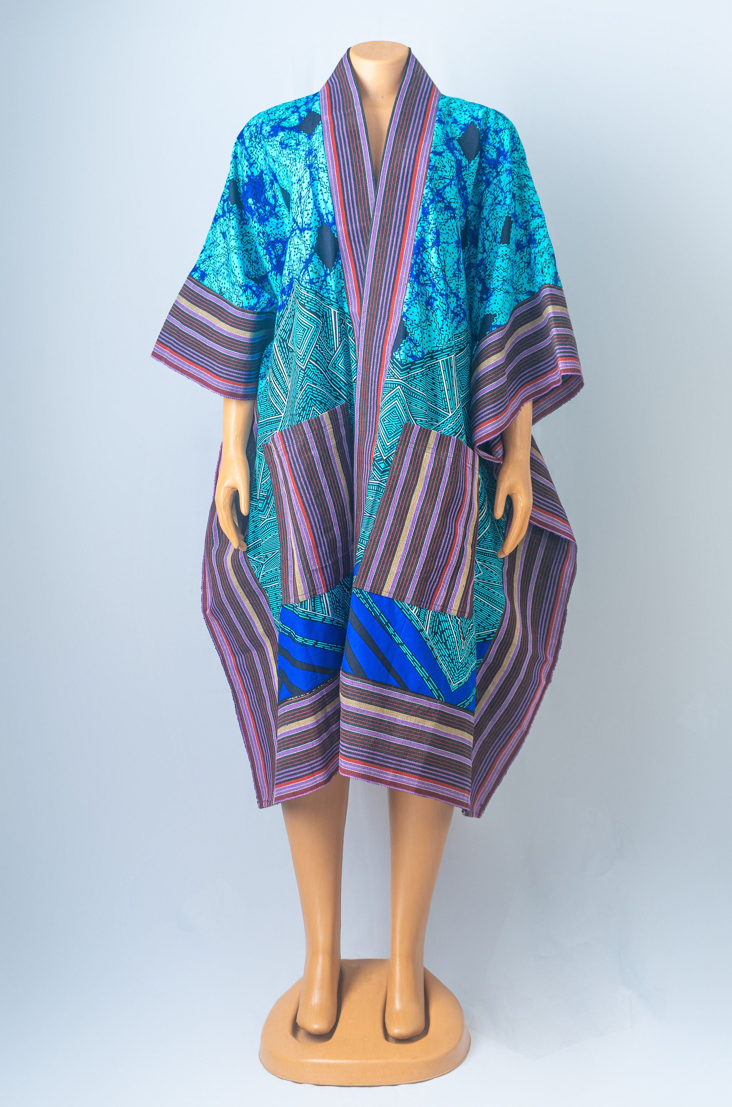 A mannequin wearing a vibrant blue, teal, and purple patchwork kimono caftan with striped details and a loose, flowing silhouette.
