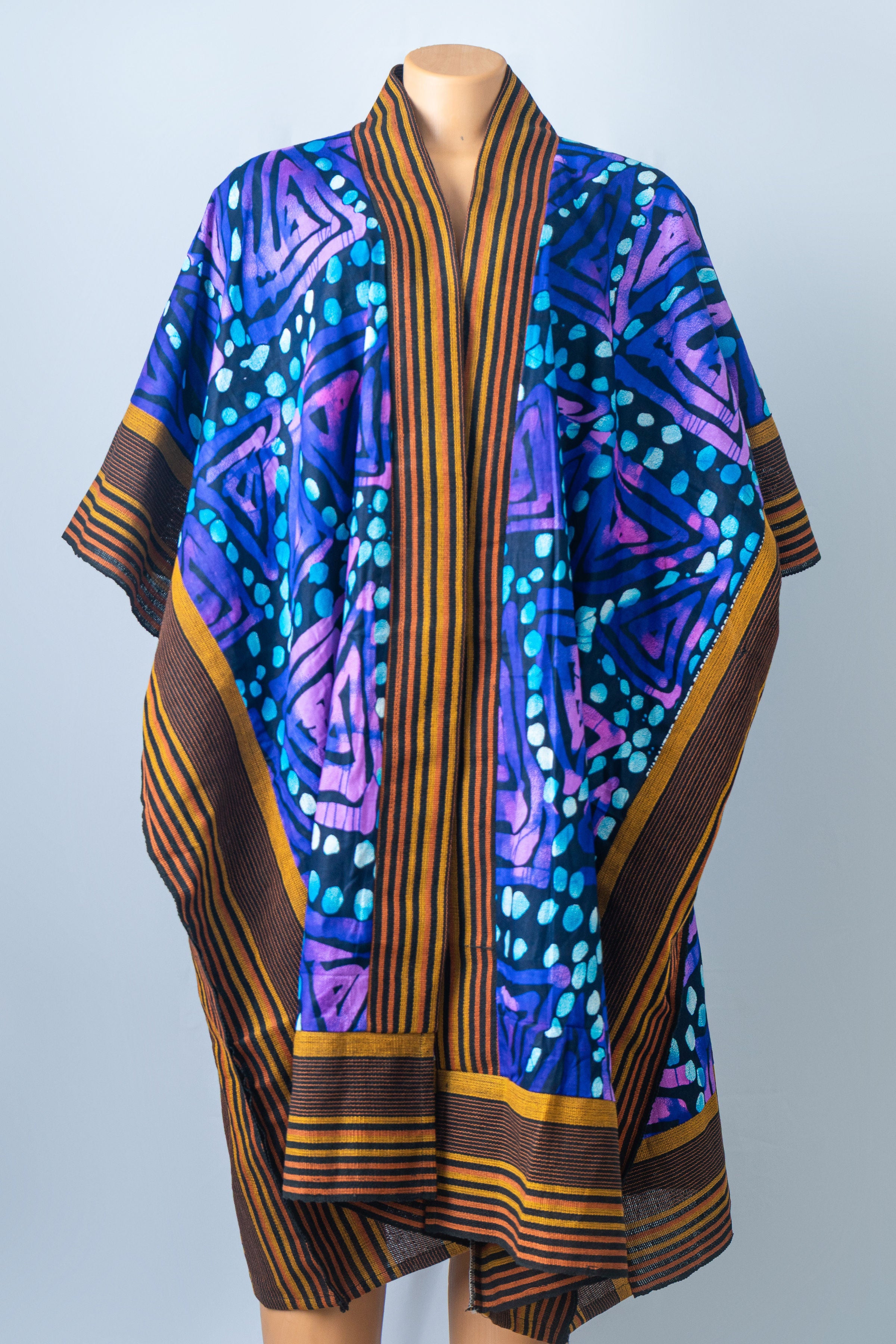 A vibrant blue, purple, and orange patterned kaftan dress with striped trim, displayed on a mannequin.