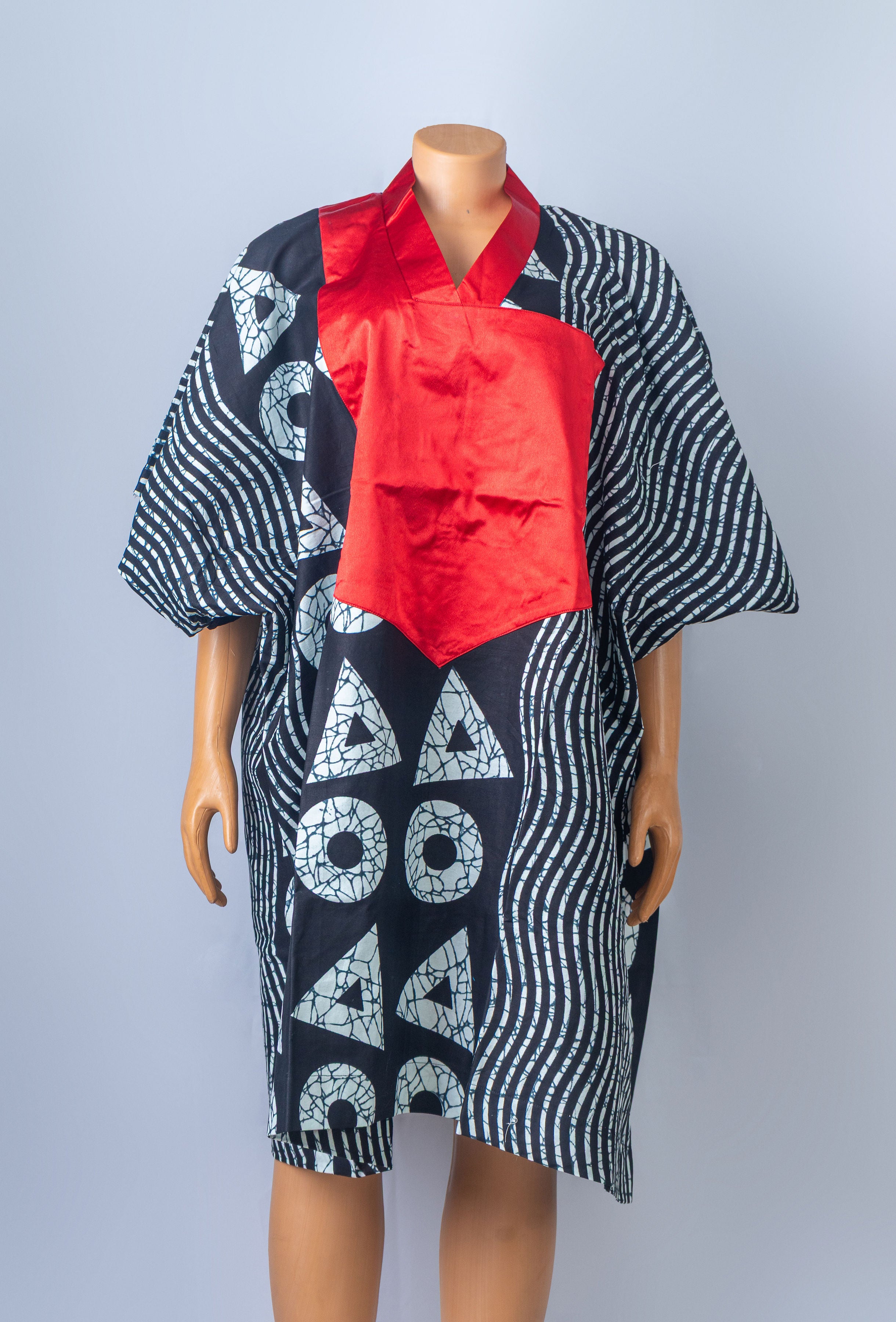 Mannequin displaying a loose-fitting black and white geometric print kimono dress with a prominent red V-neck design.