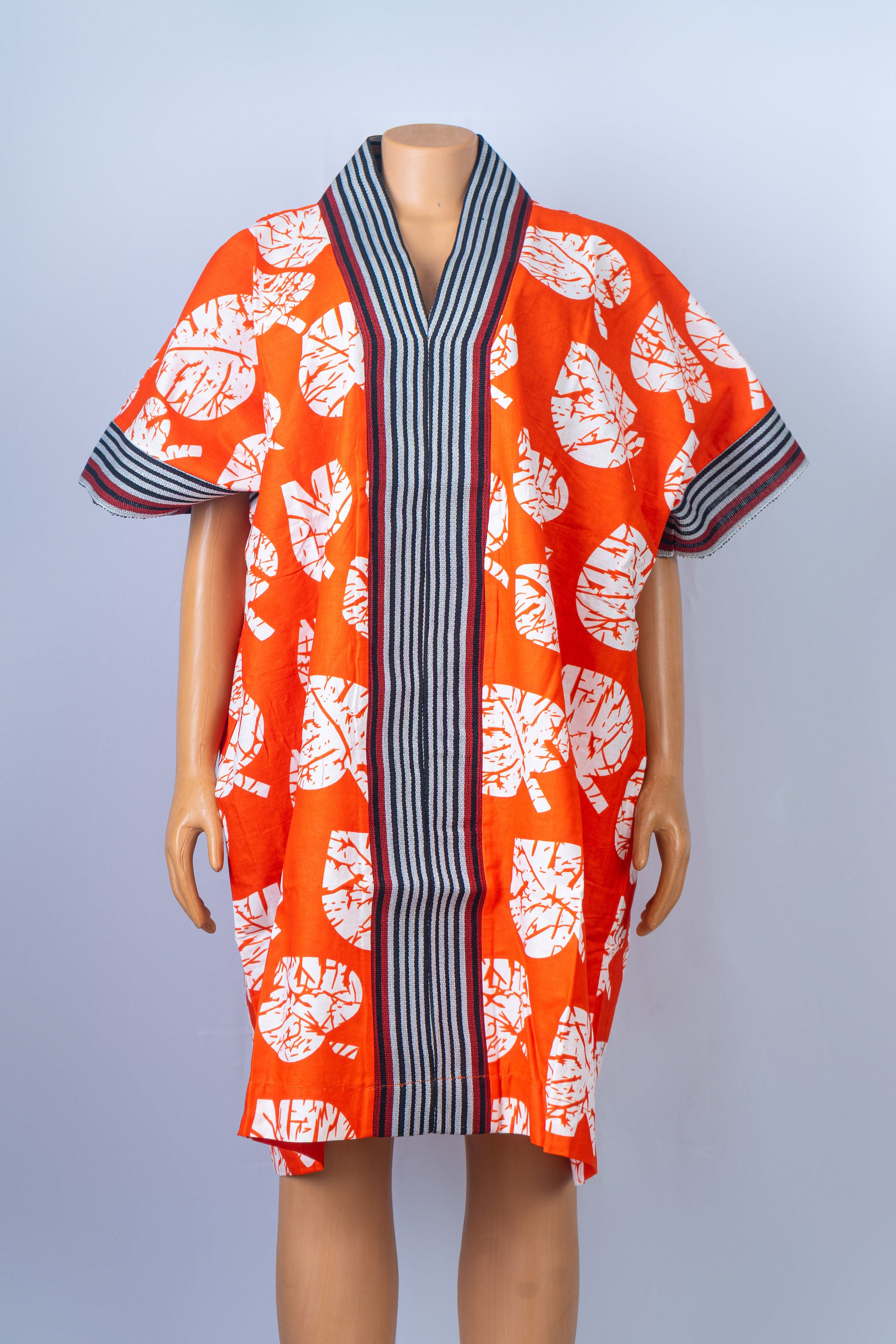 Bright orange kaftan dress with white leaf print and striped V-neck collar on a mannequin
