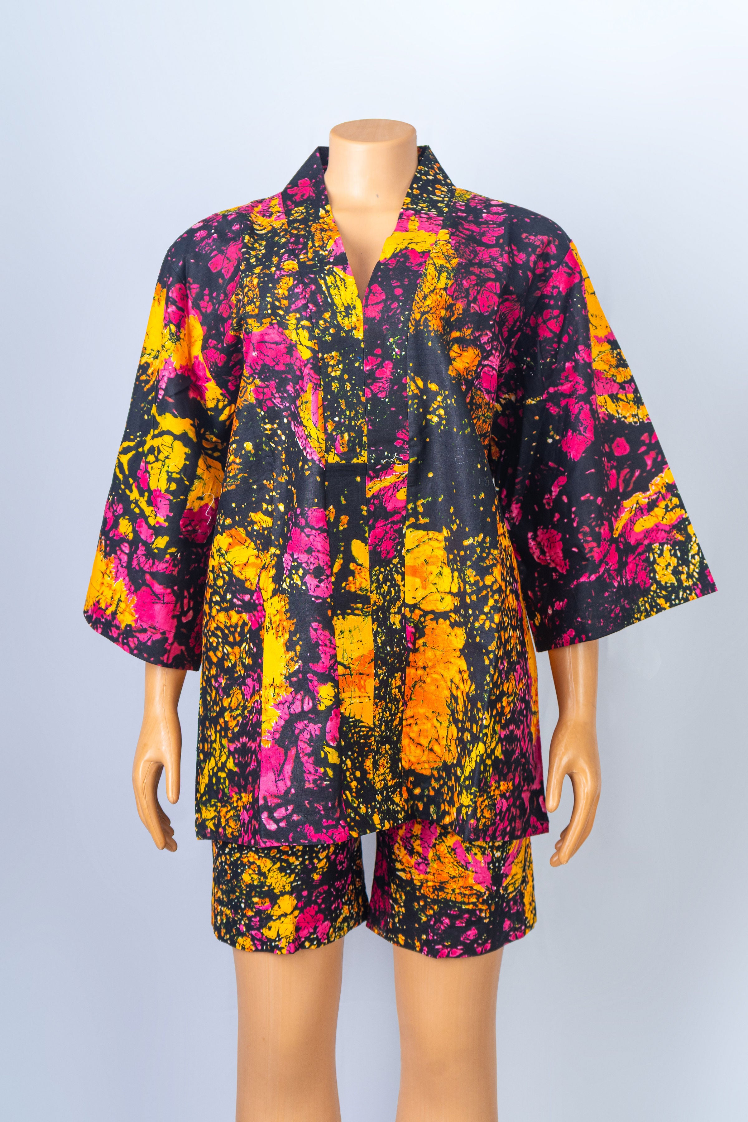 Mannequin wearing a vibrant black, yellow, pink, and orange batik print kimono-style top and matching shorts set.